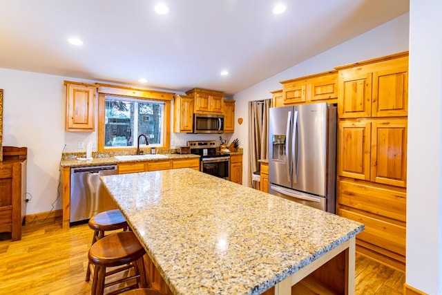 kitchen with appliances with stainless steel finishes, sink, light wood-type flooring, and a center island