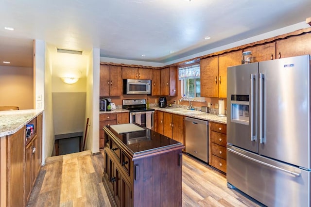 kitchen with light stone countertops, sink, stainless steel appliances, and light hardwood / wood-style floors