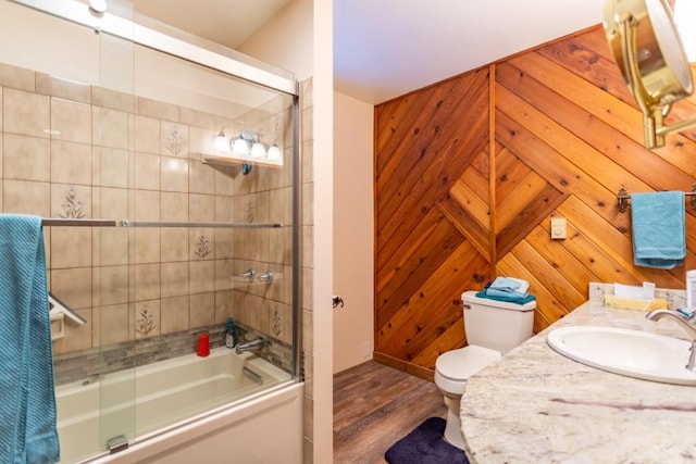 full bathroom with vanity, wood walls, bath / shower combo with glass door, toilet, and hardwood / wood-style flooring