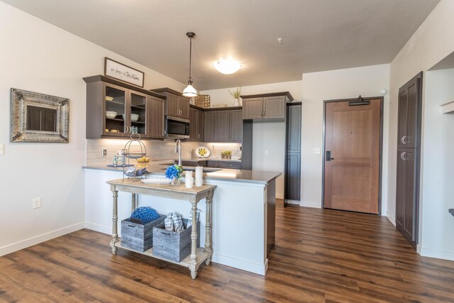 kitchen featuring kitchen peninsula, tasteful backsplash, dark brown cabinets, decorative light fixtures, and dark hardwood / wood-style flooring