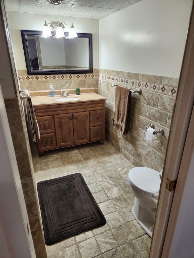 bathroom featuring tile flooring, large vanity, toilet, and tile walls