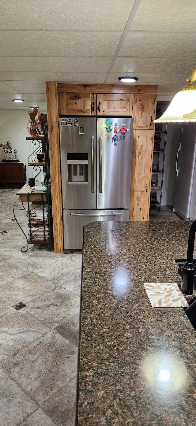 kitchen with dark stone counters, stainless steel fridge, stainless steel fridge with ice dispenser, and a drop ceiling