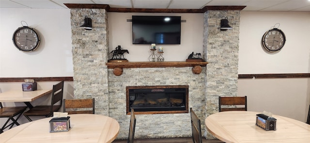 living room featuring a drop ceiling and a stone fireplace