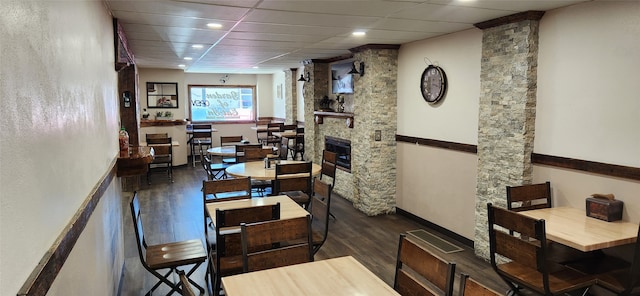 dining space with dark hardwood / wood-style floors, ornate columns, and a stone fireplace