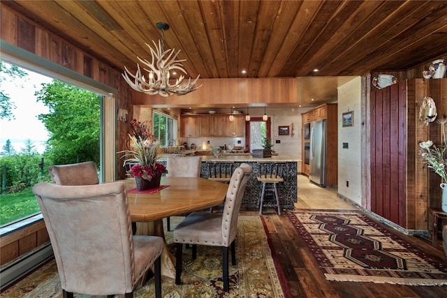 dining room with wooden ceiling, an inviting chandelier, a baseboard heating unit, wood walls, and light hardwood / wood-style floors