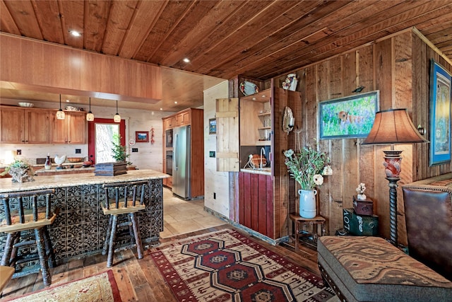 kitchen with wooden ceiling, wooden walls, light wood-type flooring, kitchen peninsula, and stainless steel refrigerator