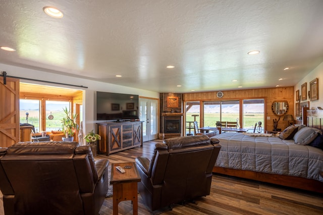 bedroom featuring a barn door, wood walls, multiple windows, and dark hardwood / wood-style floors