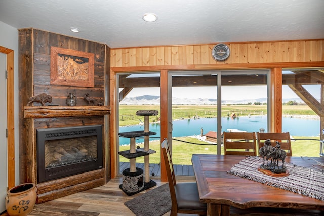 dining space featuring wood walls, a water view, a healthy amount of sunlight, and hardwood / wood-style flooring