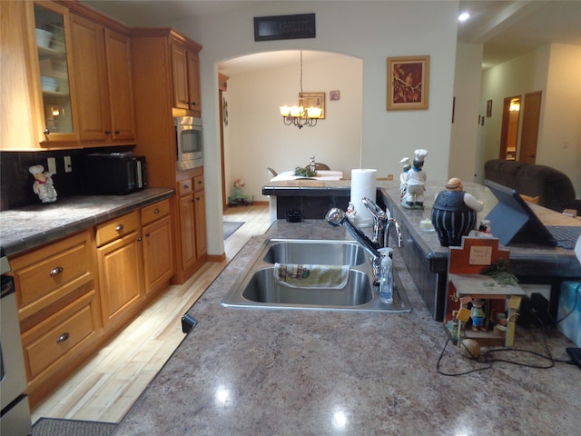 kitchen featuring sink, stainless steel microwave, light hardwood / wood-style floors, tasteful backsplash, and a notable chandelier