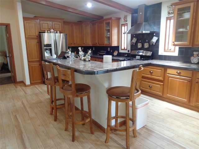 kitchen with light hardwood / wood-style floors, wall chimney range hood, stove, a breakfast bar, and stainless steel refrigerator with ice dispenser