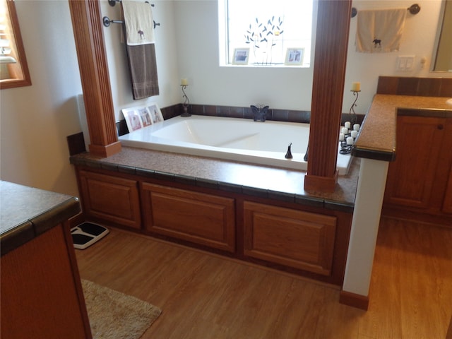 bathroom with vanity, wood-type flooring, and a bath to relax in