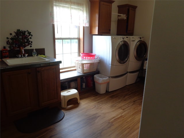 clothes washing area featuring sink, cabinets, washer and clothes dryer, and hardwood / wood-style flooring