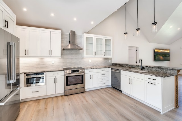 kitchen with appliances with stainless steel finishes, sink, light wood-type flooring, white cabinets, and wall chimney range hood