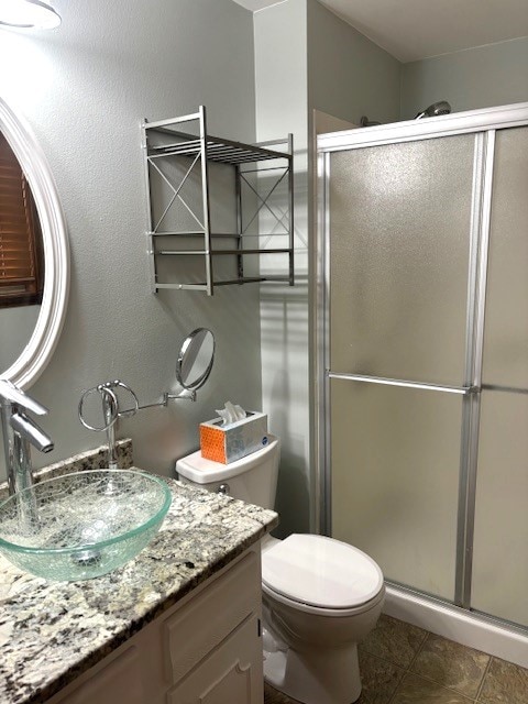 bathroom with toilet, tile floors, vanity, and a shower with shower door