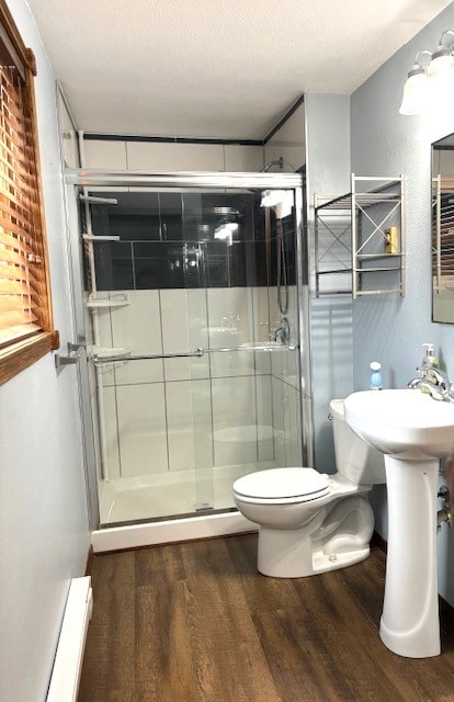 bathroom with a baseboard radiator, toilet, hardwood / wood-style floors, a textured ceiling, and walk in shower