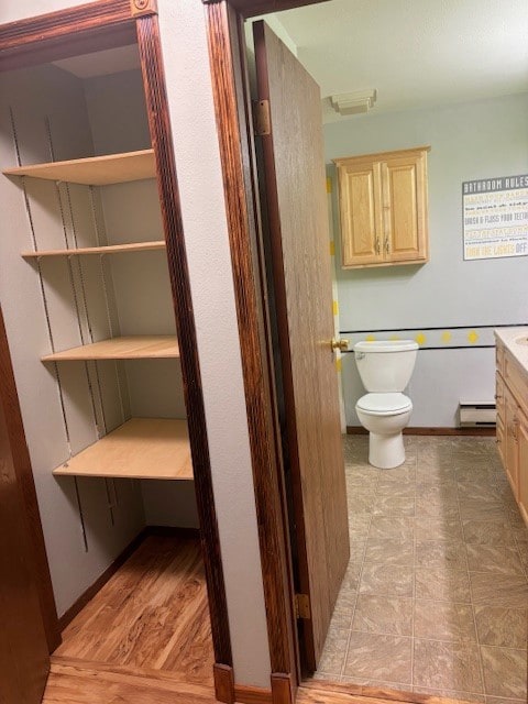 bathroom with a baseboard heating unit, toilet, vanity, and wood-type flooring