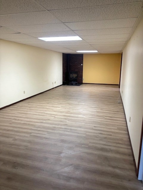 basement with light hardwood / wood-style floors, a drop ceiling, and a wood stove