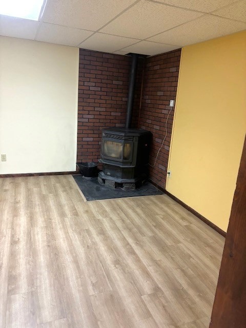 unfurnished living room with a paneled ceiling, brick wall, a wood stove, and light wood-type flooring