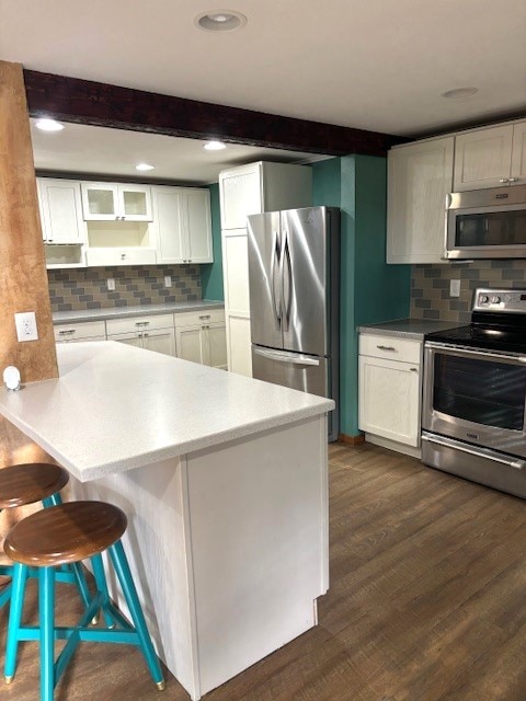 kitchen featuring dark hardwood / wood-style floors, white cabinets, appliances with stainless steel finishes, and a kitchen breakfast bar