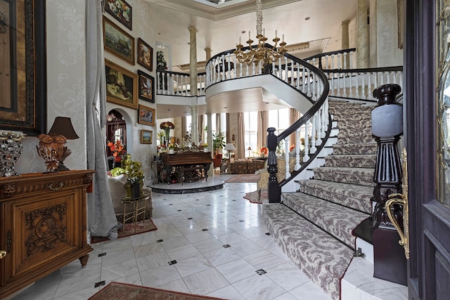 tiled entryway featuring a chandelier, decorative columns, a high ceiling, and crown molding