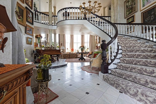 tiled entryway featuring a chandelier, decorative columns, and a high ceiling