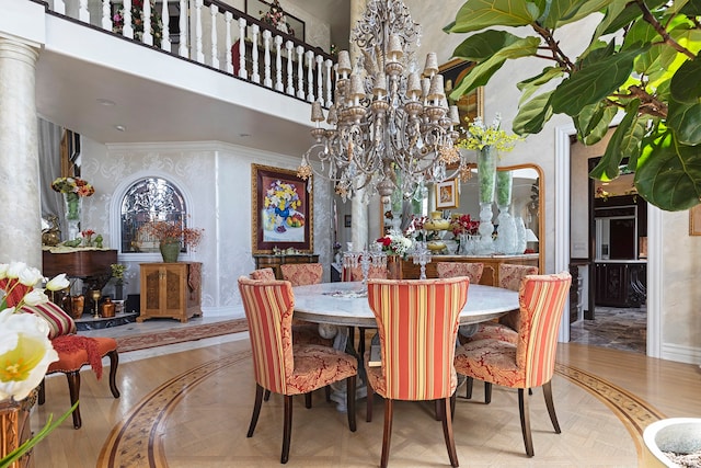 dining room featuring a chandelier, a high ceiling, light parquet flooring, crown molding, and decorative columns