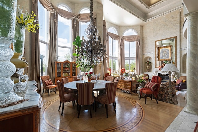 tiled dining room featuring a notable chandelier, crown molding, decorative columns, and a towering ceiling