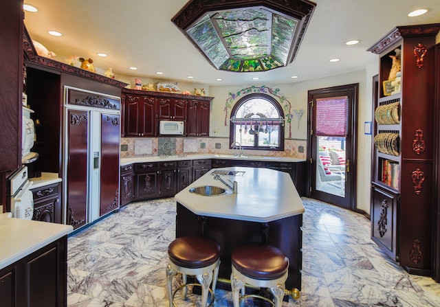 kitchen featuring a kitchen island, built in appliances, light tile floors, backsplash, and sink