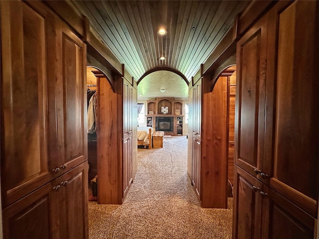 hallway featuring light carpet, wooden ceiling, and wood walls