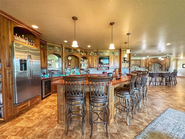 kitchen with a center island, beverage cooler, stainless steel fridge, a textured ceiling, and decorative light fixtures