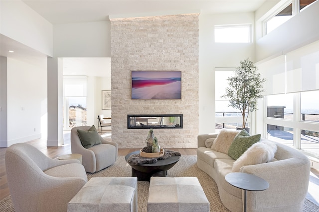 living room featuring light wood-type flooring, a high ceiling, a fireplace, and a healthy amount of sunlight