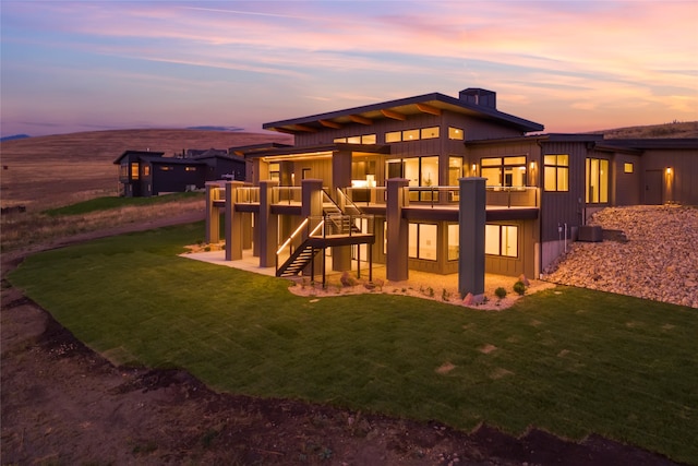 back house at dusk featuring a balcony and a lawn