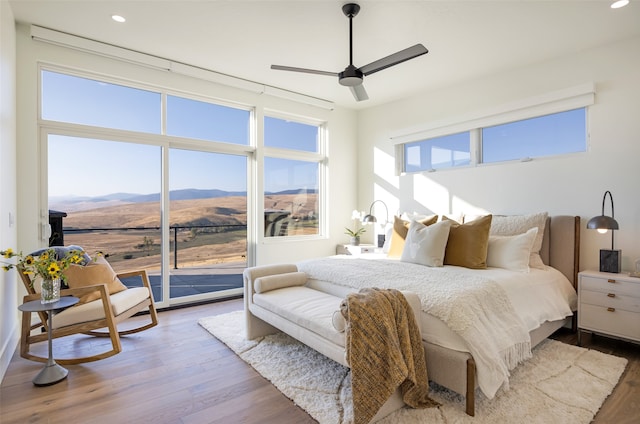 bedroom featuring a mountain view, hardwood / wood-style floors, access to exterior, and ceiling fan