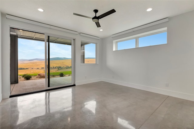 spare room with ceiling fan, a mountain view, and concrete flooring