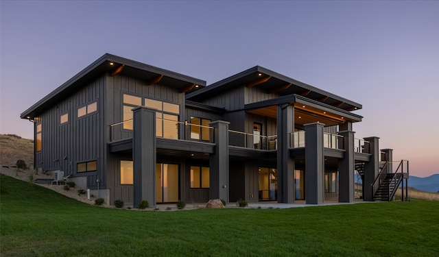 back house at dusk featuring a lawn and a balcony