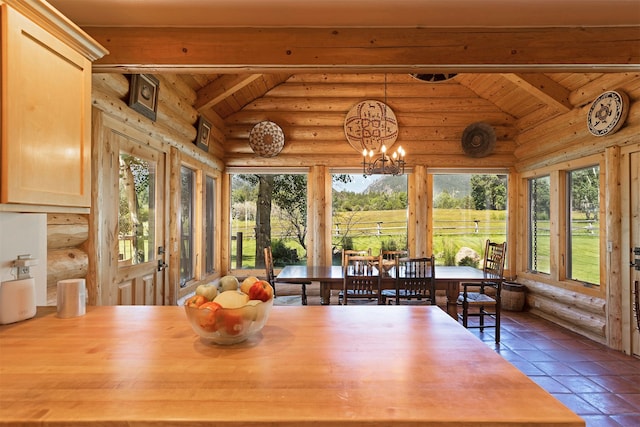 dining room with lofted ceiling with beams, rustic walls, and a notable chandelier