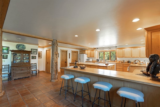 kitchen with light brown cabinets, butcher block countertops, dark tile flooring, a kitchen breakfast bar, and white appliances