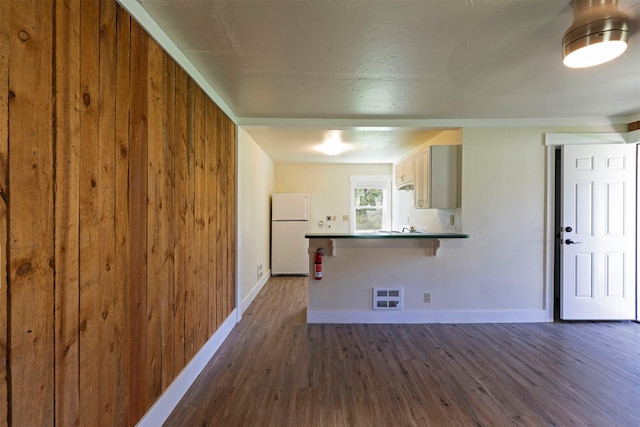 kitchen with dark wood-type flooring, wooden walls, and white fridge