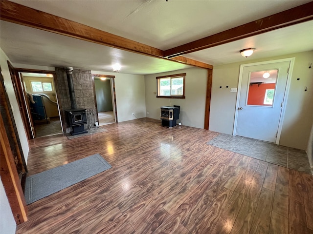 unfurnished living room with dark wood-type flooring, a wood stove, and beam ceiling