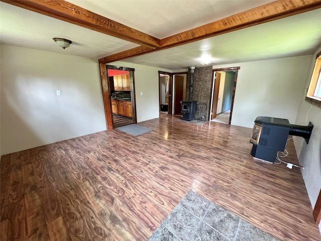 empty room with dark hardwood / wood-style flooring, beam ceiling, and a wood stove