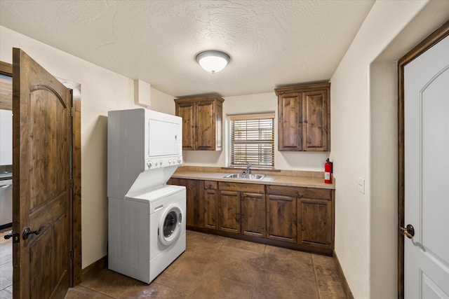 laundry area with dark tile flooring, a textured ceiling, stacked washer / drying machine, and sink