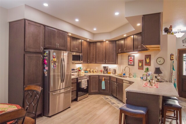 kitchen with appliances with stainless steel finishes, light hardwood / wood-style flooring, sink, dark brown cabinetry, and a kitchen breakfast bar