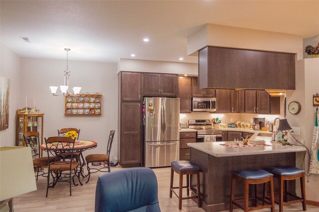 kitchen with a breakfast bar, dark brown cabinets, kitchen peninsula, light hardwood / wood-style floors, and appliances with stainless steel finishes