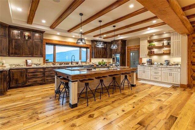 kitchen with beamed ceiling, a breakfast bar area, light hardwood / wood-style floors, a mountain view, and an island with sink