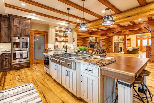 kitchen featuring log walls, stainless steel appliances, light hardwood / wood-style floors, beamed ceiling, and hanging light fixtures