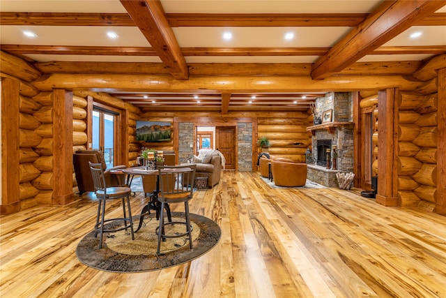 dining space featuring log walls, beamed ceiling, light wood-type flooring, and a stone fireplace