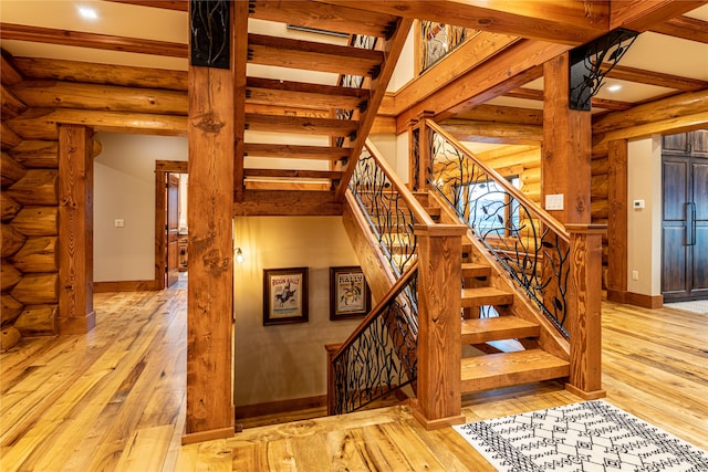 stairway featuring log walls, light hardwood / wood-style flooring, and beam ceiling