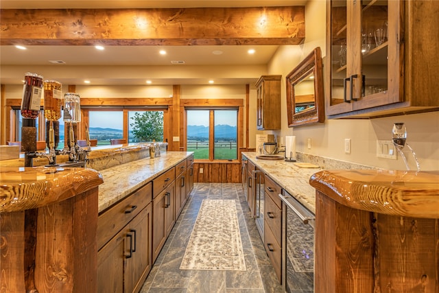 kitchen with a mountain view, dark tile patterned floors, light stone counters, and beamed ceiling