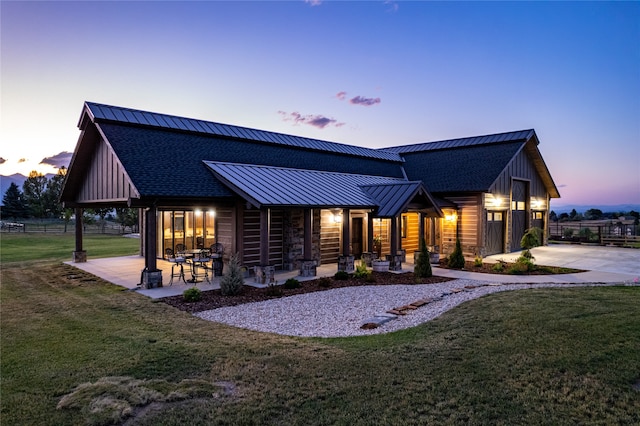 back house at dusk with a patio and a lawn