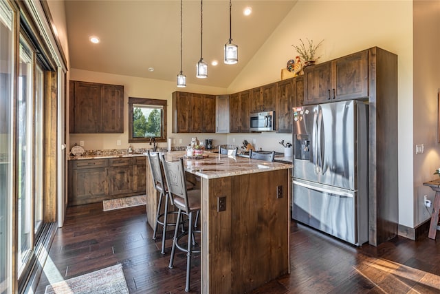 kitchen with pendant lighting, dark hardwood / wood-style floors, a kitchen island, appliances with stainless steel finishes, and a kitchen breakfast bar